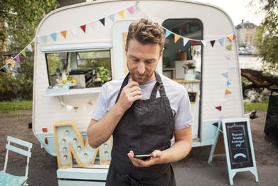 Male owner using smart phone while standing on street against food truck