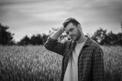 Young man looking away on field against sky