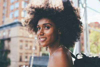 Side view portrait of happy young woman with afro hairstyle carrying backpack in city