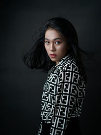 Portrait of young woman standing against black background