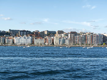 Sea by buildings in city against sky