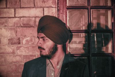 Portrait of young man looking away against brick wall