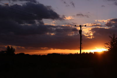 Low angle view of silhouette electricity pylon on field against sky