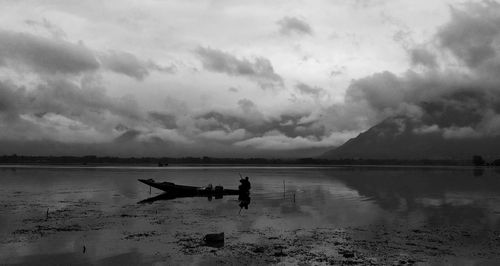 Silhouette people on boat at lake against sky