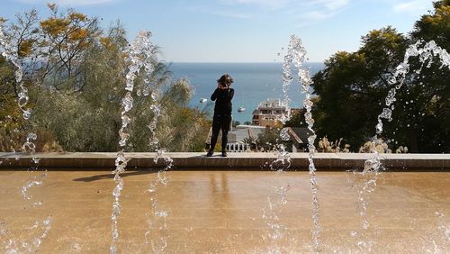 Woman standing on fountain in park against sky