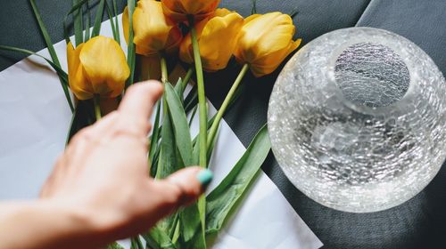 Cropped hand of woman reaching yellow tulips on table