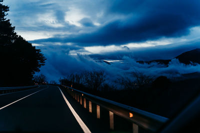 Road by trees against sky at dusk