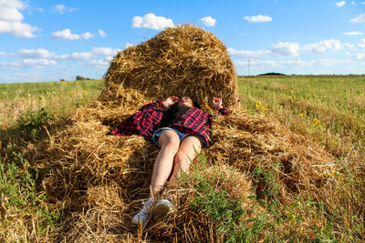 Woman with hay bales on field against sky