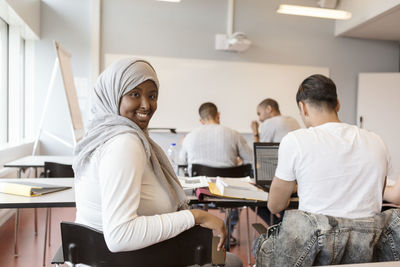 Portrait of smiling student in hijab sitting with friends in classroom at university