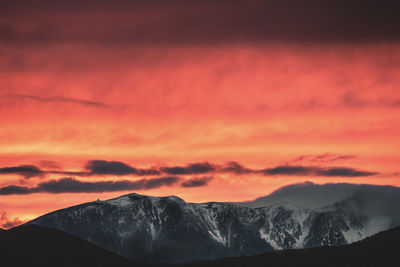 Scenic view of snowcapped mountains against orange sky