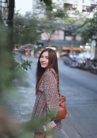 Portrait of smiling young woman standing in city