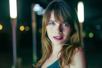 Close-up portrait of young woman standing outdoors at night