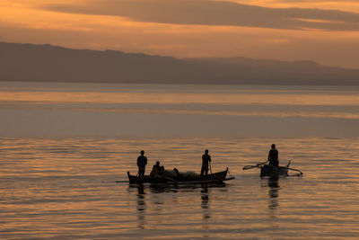 Silhouette people in boat on sea against sky during sunset