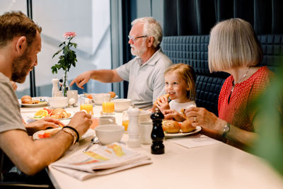 Smiling girl looking at father while having food with grandparents at restaurant