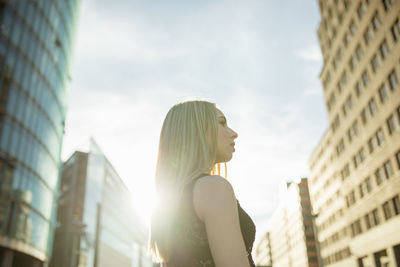 Side view of beautiful young woman standing against buildings in city