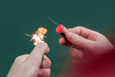 Cropped image of hand holding sparkler against sky