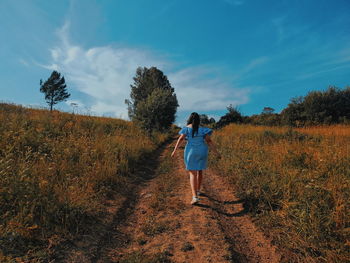 Rear view of woman walking on field against sky