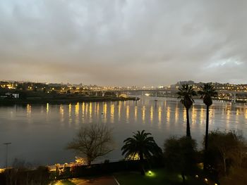 Illuminated city by river against sky