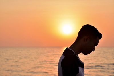 Side view of man standing at beach against sky during sunset