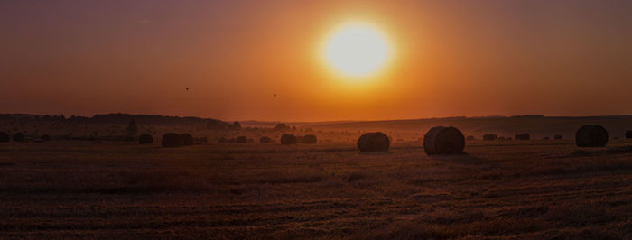 Hay bales on field against sky during sunset