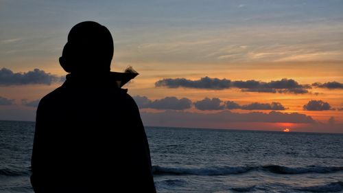 Silhouette man looking at sea against sky during sunset