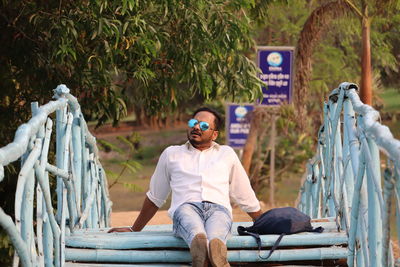 Full length of man sitting by sunglasses in wodden brize