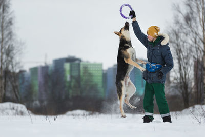 Man playing with dog in snow against sky