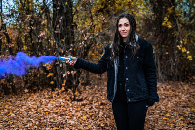 Young woman holding distress flare while standing in forest during autumn