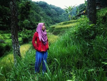 Young woman wearing hijab while standing on grassy field in forest