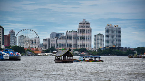 Boats in river by buildings in city against sky