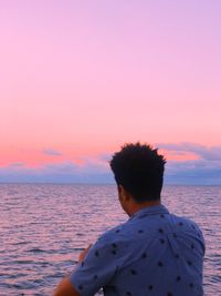 Rear view of man by sea against sky during sunset