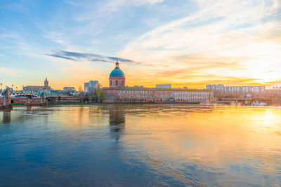 View of buildings by river against sky in city