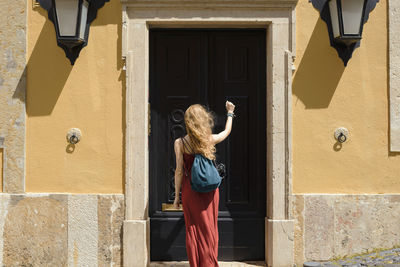 Rear view of woman with backpack knocking door