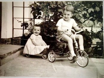 Boy riding tricycle while sister sitting in wagon at yard