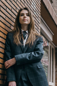 Portrait of beautiful young woman standing against brick wall