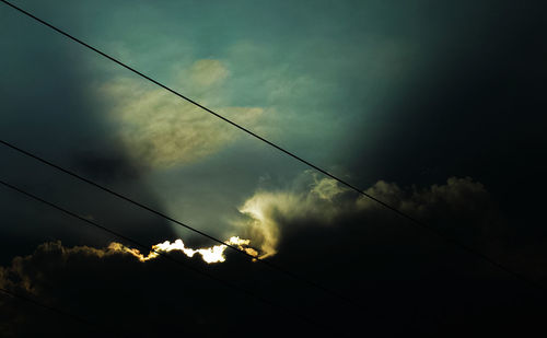 Low angle view of electricity pylon against cloudy sky