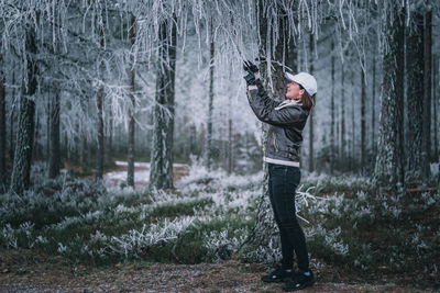 Woman standing by tree trunk in forest during winter