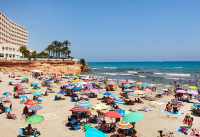 People at beach against clear blue sky during summer