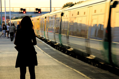 Rear view of silhouette woman standing on railroad station by train