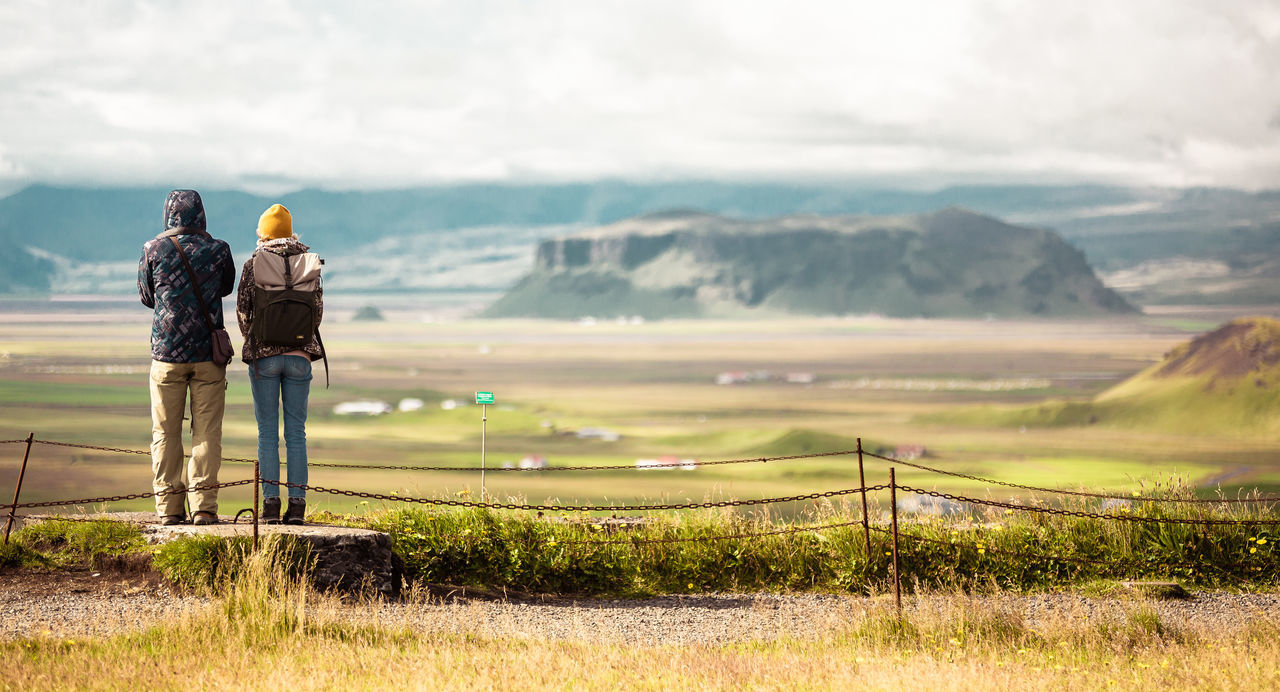 rear view, real people, sky, mountain, grass, nature, cloud - sky, leisure activity, adult, full length, landscape, standing, men, environment, beauty in nature, scenics - nature, day, two people, lifestyles, activity, outdoors, couple - relationship, looking at view