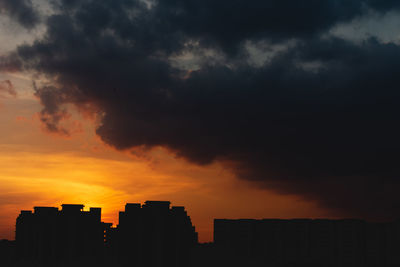 Silhouette buildings against dramatic sky during sunset