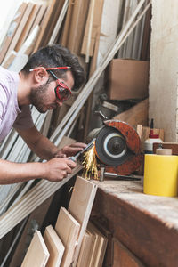 Male craftsperson sharpening chisel on grinder while working in workshop