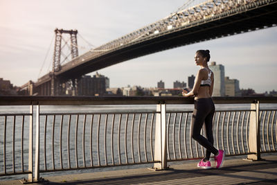 Thoughtful jogger standing by railing on promenade with williamsburg bridge