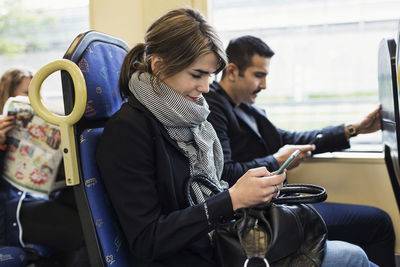 Young woman using mobile phone while sitting with man in tram