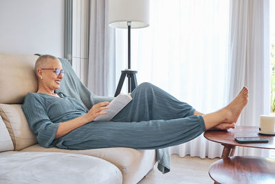Woman reading book while relaxing on sofa at home