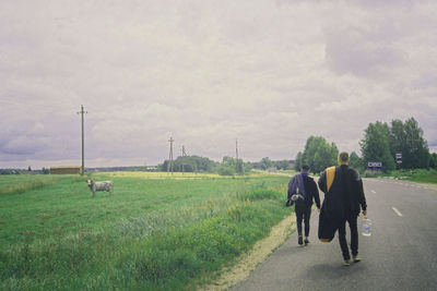 Rear view of people walking on road against sky