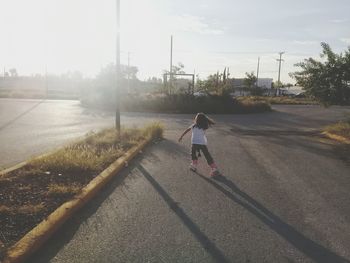 Rear view of girl inline skating on road during sunset