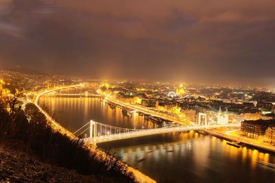 Illuminated bridge over river in city at night