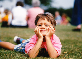 Portrait of boy with hand on chin lying on field at park