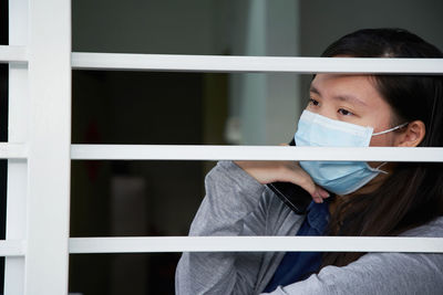 Portrait of young woman with face mask  behind window